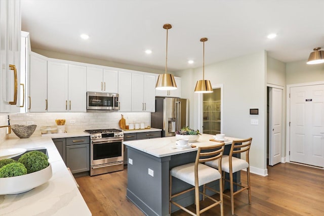 kitchen with a center island, decorative light fixtures, light stone counters, white cabinetry, and stainless steel appliances