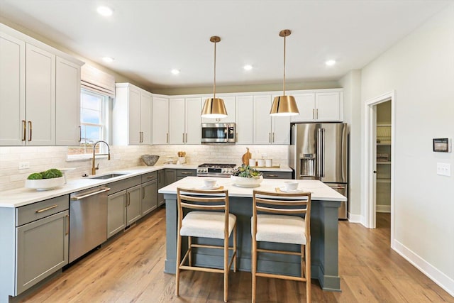 kitchen featuring appliances with stainless steel finishes, sink, gray cabinets, a kitchen island, and hanging light fixtures