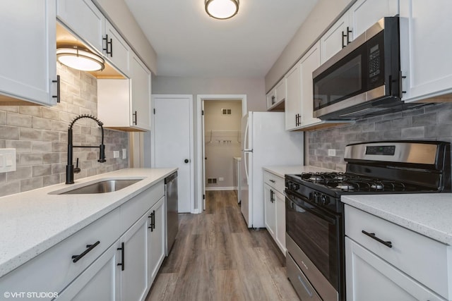 kitchen featuring white cabinetry, sink, light hardwood / wood-style flooring, decorative backsplash, and appliances with stainless steel finishes