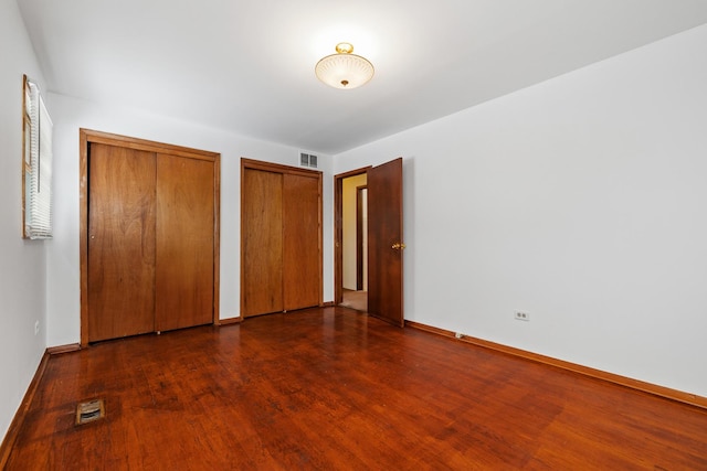 unfurnished bedroom with dark hardwood / wood-style flooring and multiple closets