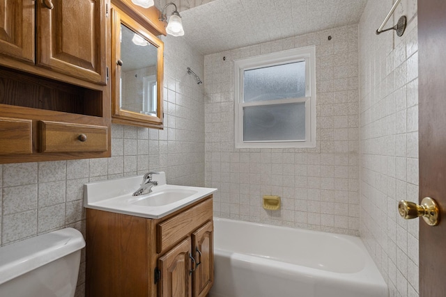 full bathroom with tiled shower / bath, vanity, tile walls, and toilet