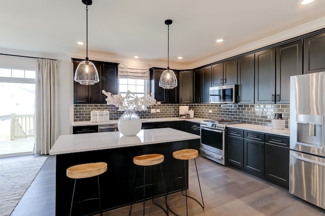 kitchen featuring wood-type flooring, stainless steel appliances, a kitchen island, and hanging light fixtures