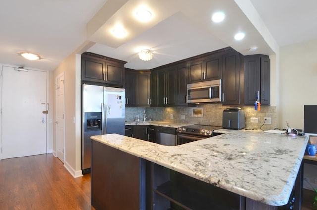 kitchen featuring dark brown cabinetry, light stone countertops, dark wood-type flooring, kitchen peninsula, and appliances with stainless steel finishes