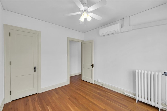 unfurnished room featuring ceiling fan, radiator heating unit, hardwood / wood-style floors, and a wall unit AC