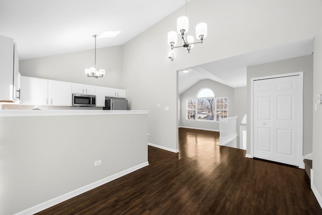 kitchen with vaulted ceiling with skylight, stainless steel appliances, decorative light fixtures, an inviting chandelier, and white cabinetry