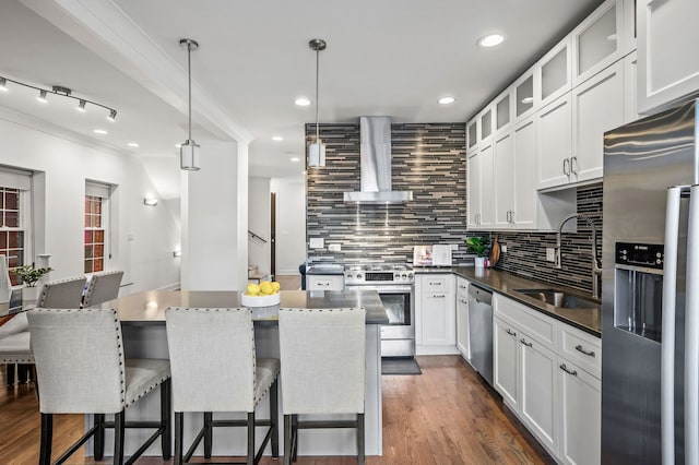 kitchen with hanging light fixtures, sink, white cabinets, stainless steel appliances, and wall chimney exhaust hood