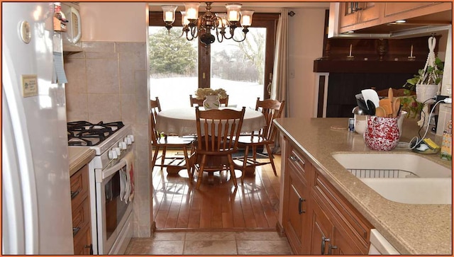 kitchen featuring an inviting chandelier, white appliances, sink, and light stone counters