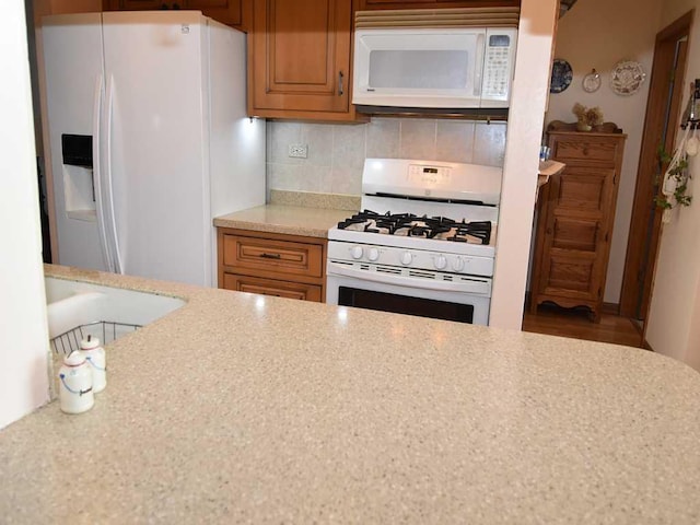 kitchen featuring light stone counters, backsplash, and white appliances