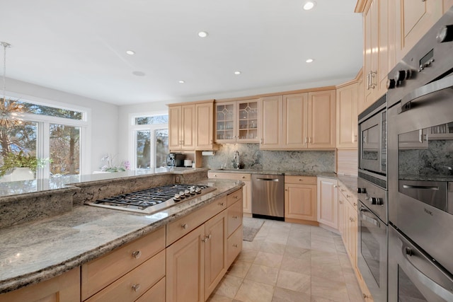 kitchen with appliances with stainless steel finishes, decorative backsplash, light brown cabinetry, light stone countertops, and sink