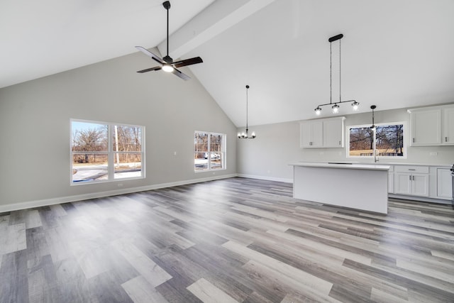 unfurnished living room with beam ceiling, plenty of natural light, light hardwood / wood-style floors, and ceiling fan with notable chandelier