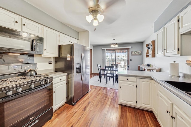 kitchen with light hardwood / wood-style floors, ceiling fan with notable chandelier, white cabinets, and black appliances