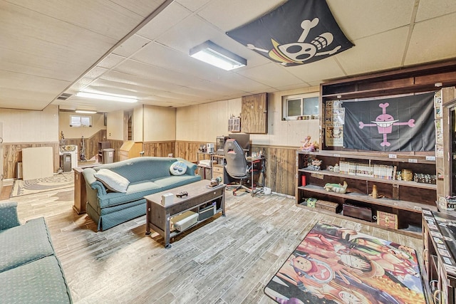 living room featuring light hardwood / wood-style flooring, wood walls, and a paneled ceiling