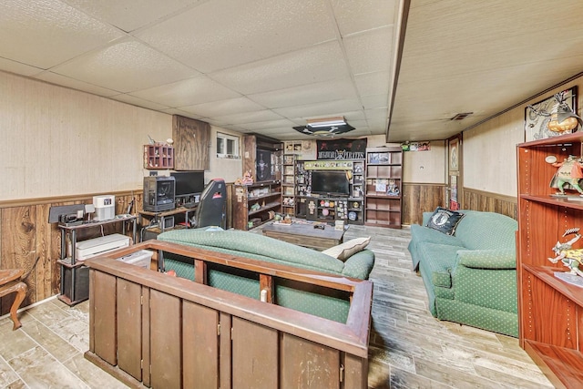 living room with a drop ceiling, wooden walls, and light wood-type flooring