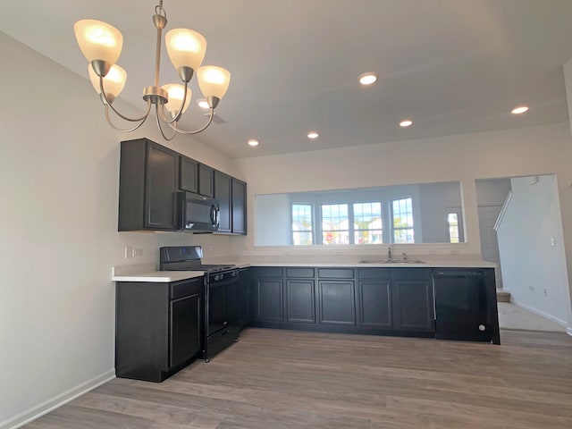 kitchen with light wood-type flooring, sink, black appliances, decorative light fixtures, and a notable chandelier