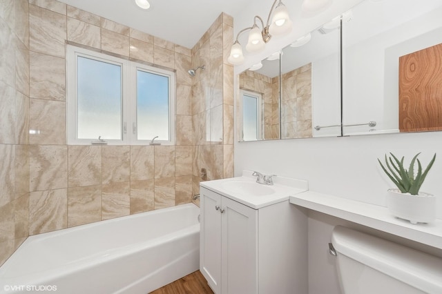 full bathroom featuring hardwood / wood-style floors, tiled shower / bath combo, vanity, and toilet