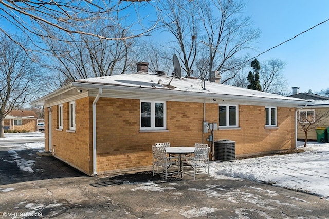 snow covered back of property featuring central AC unit