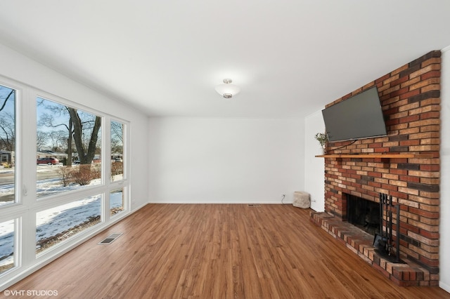 unfurnished living room featuring a healthy amount of sunlight, a brick fireplace, and hardwood / wood-style flooring