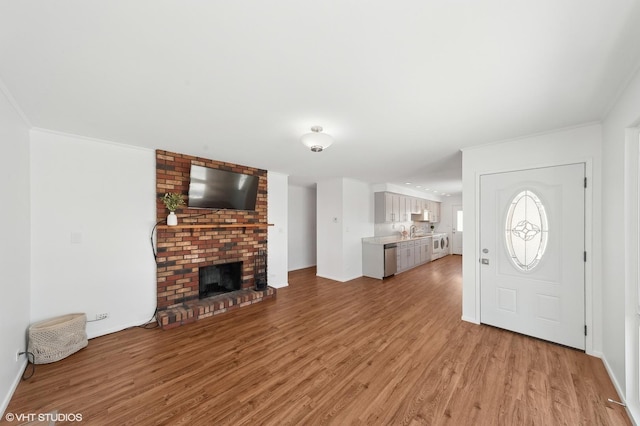 entryway featuring a brick fireplace, sink, crown molding, and light hardwood / wood-style flooring