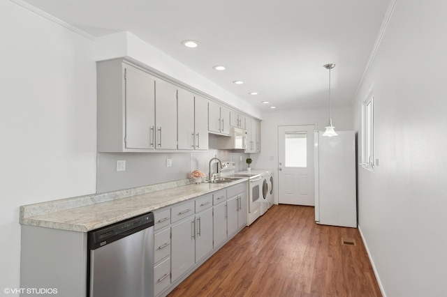 kitchen featuring white appliances, washing machine and dryer, decorative light fixtures, sink, and hardwood / wood-style flooring