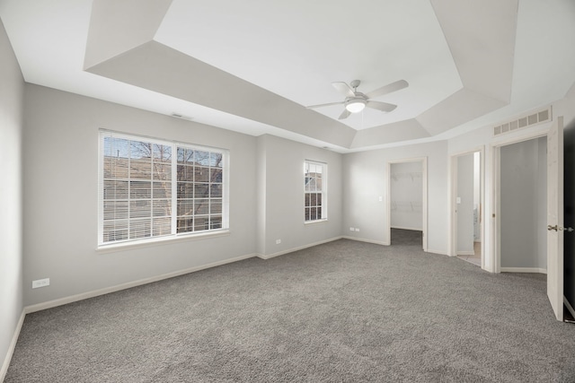 unfurnished bedroom featuring carpet, ceiling fan, multiple windows, and a tray ceiling