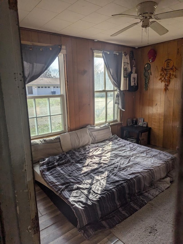 bedroom with ceiling fan, wood walls, and hardwood / wood-style flooring