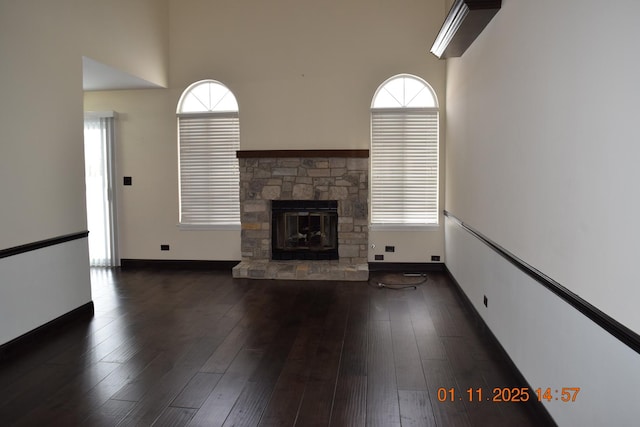 unfurnished living room featuring plenty of natural light, a stone fireplace, and dark wood-type flooring