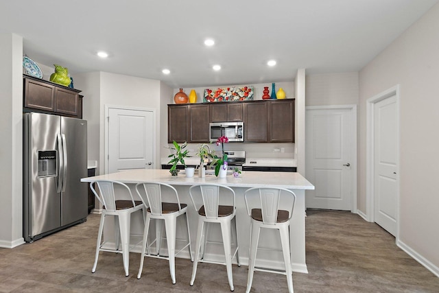 kitchen with a kitchen island with sink, appliances with stainless steel finishes, a kitchen breakfast bar, and dark brown cabinets