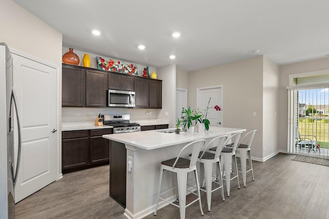 kitchen featuring dark brown cabinetry, appliances with stainless steel finishes, a kitchen bar, an island with sink, and light hardwood / wood-style flooring