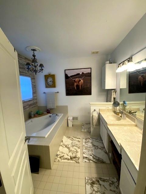 bathroom featuring vanity, a relaxing tiled tub, and an inviting chandelier