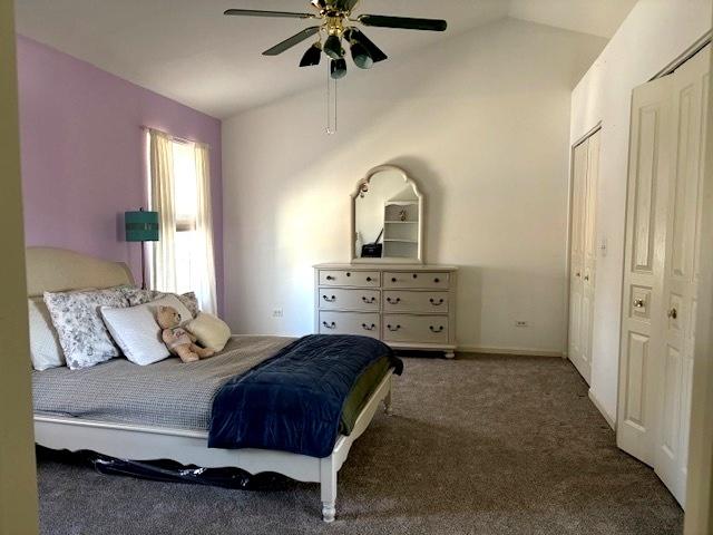 carpeted bedroom with two closets, vaulted ceiling, and ceiling fan