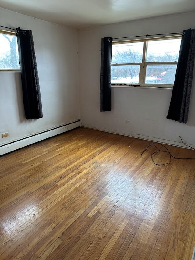 unfurnished room with a baseboard heating unit, a wealth of natural light, and light hardwood / wood-style floors