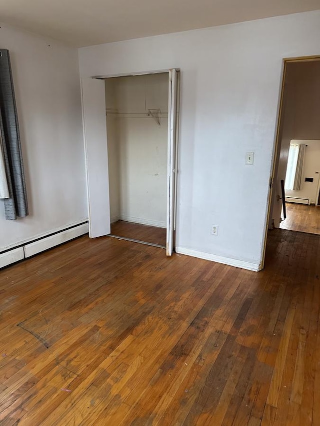 unfurnished bedroom featuring dark wood-type flooring, a closet, and baseboard heating