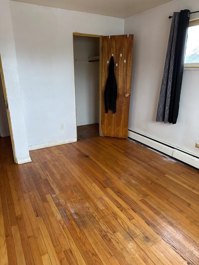 unfurnished bedroom with light hardwood / wood-style floors, baseboard heating, and a closet