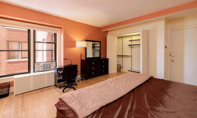 bedroom featuring a closet, light wood-type flooring, radiator heating unit, and cooling unit