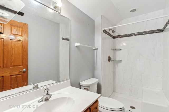 bathroom with toilet, a tile shower, vanity, and lofted ceiling