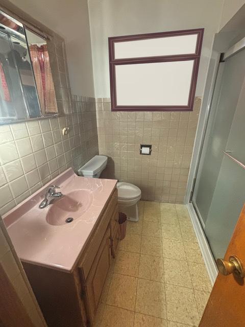 bathroom featuring vanity, a shower with door, toilet, and tile walls