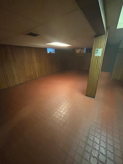 basement with a paneled ceiling and wood walls