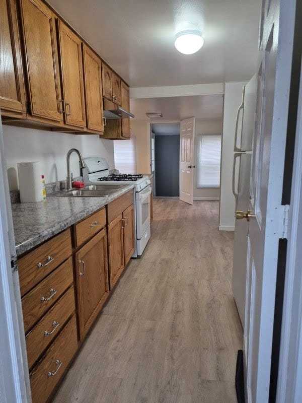 kitchen with white range with gas cooktop, sink, dark stone counters, and light wood-type flooring