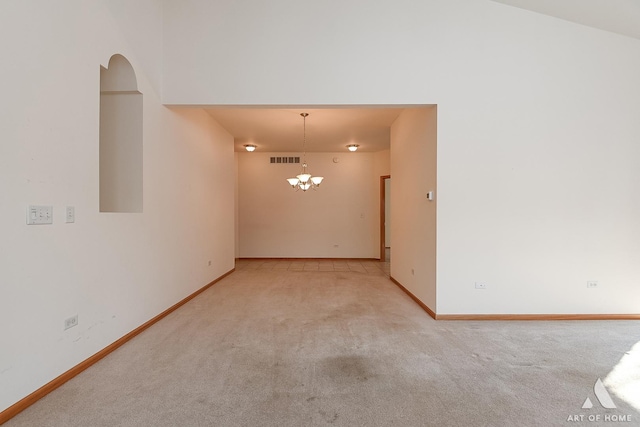 spare room featuring light carpet and a chandelier