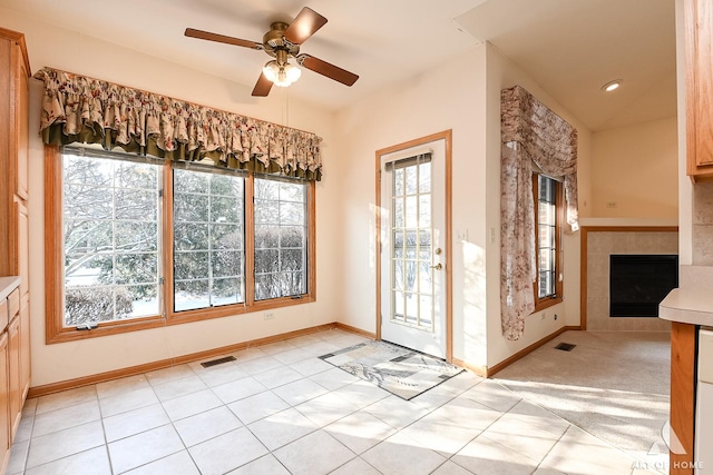 interior space with a tiled fireplace, ceiling fan, and light tile patterned flooring