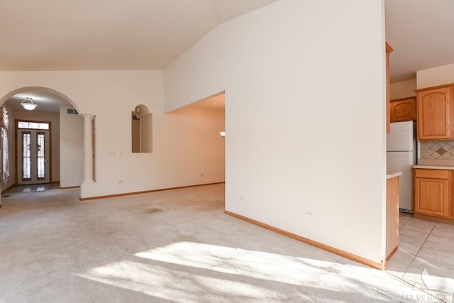 unfurnished living room featuring light carpet, ornate columns, and lofted ceiling