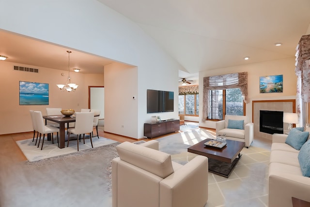 living room with high vaulted ceiling, ceiling fan with notable chandelier, and a tile fireplace