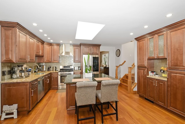 kitchen with wall chimney range hood, appliances with stainless steel finishes, a skylight, a kitchen breakfast bar, and a kitchen island