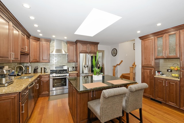 kitchen featuring sink, dark stone counters, a center island, stainless steel appliances, and wall chimney range hood