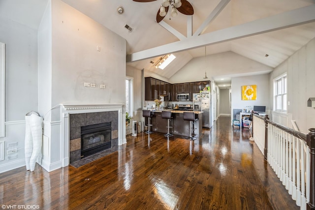 living room featuring a fireplace, ceiling fan, vaulted ceiling with skylight, and dark hardwood / wood-style floors