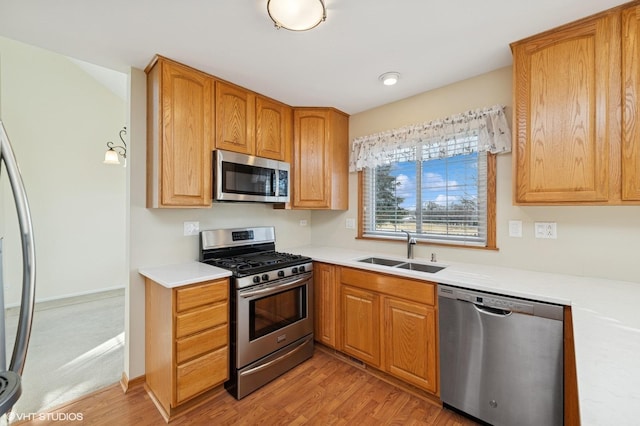 kitchen featuring stainless steel appliances, a sink, baseboards, light wood-style floors, and light countertops