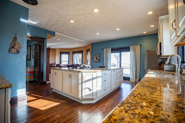 kitchen with a kitchen island, sink, white cabinets, light stone counters, and dark wood-type flooring