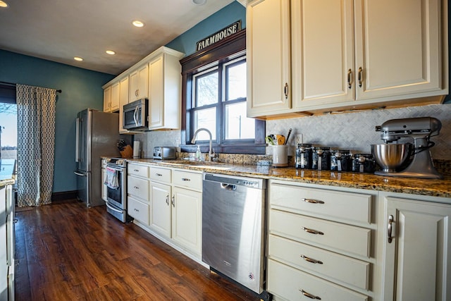 kitchen with sink, dark wood-type flooring, appliances with stainless steel finishes, dark stone countertops, and white cabinets