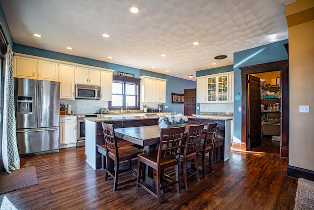 kitchen with appliances with stainless steel finishes, a kitchen bar, dark hardwood / wood-style flooring, a center island, and light stone counters