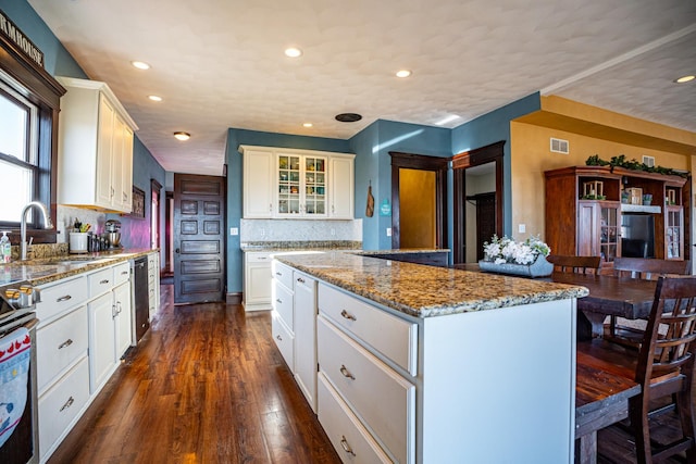 kitchen featuring dark wood-type flooring, sink, a kitchen island, dark stone counters, and white cabinets